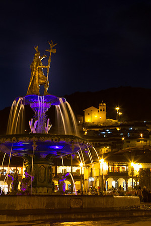 Plaza de Armas fountain at night with Church of San Cristobal on hillside behind the plaza